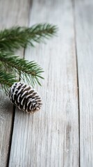 A pine cone dusted with snow rests on a wooden surface, surrounded by evergreen branch, branches.