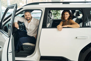 Happy couple sitting in new car in auto showroom