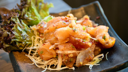 Close-up of marinated salmon poke with fresh lettuce and shredded vegetables in black ceramic dish
