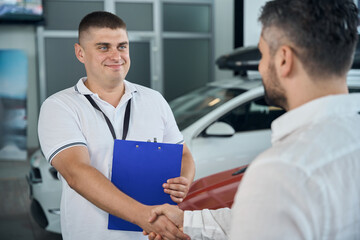 Fototapeta premium Male client shaking hands with salesman manager at car salon showroom