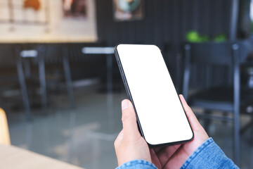 Mockup image of a woman holding and using mobile phone with blank desktop in cafe