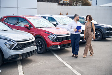 Female client talking with salesman manager at car salon showroom outdoors