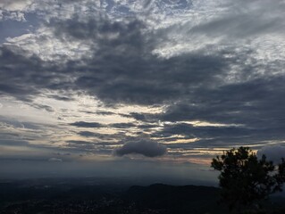 Dramatic sunset sky with layered clouds over a sprawling valley vista. A captivating view of a valley landscape at sunset, shrouded in a dramatic sky filled with layered grey and white clouds.