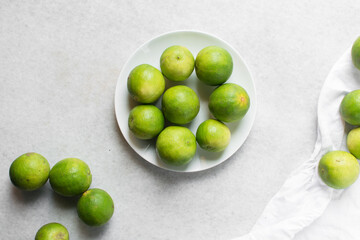 Overhead view of green limes in a white ceramic bowl, top view of organic limes in a white bowl