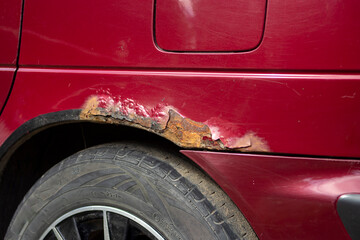 Rusty car. Red old rusty car. Fragment of a red wing of an old car. Rusty hole in metal