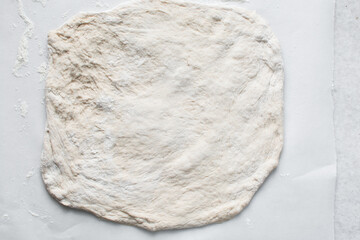 Overhead view of bread dough on parchment lined baking sheet, Shaping proofed dough on a white surface, process of making artisan bread