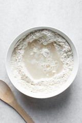 Overhead view of artisan bread dough being mixed in a white mixing bowl, top view of dry bread dough, process of making white bread