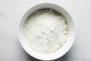 Overhead view of ingredients for making puff-puff in a white ceramic bowl, yeast flour sugar in a mixing bowl, process of making puff-puff
