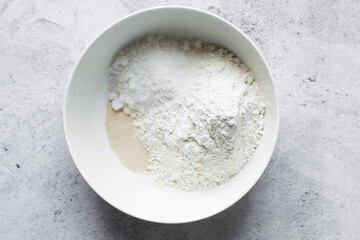 Overhead view of ingredients for making puff-puff in a white ceramic bowl, yeast flour sugar in a...