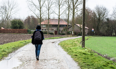 Woman walking over paved path in the Hageland around Zoutleeuw in winter, Flanders, Belgium.