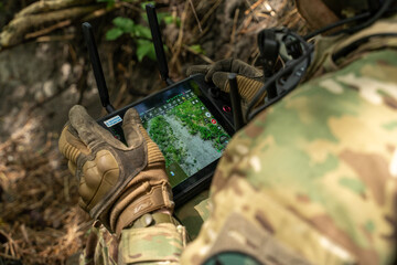 A soldier in tactical gear operates a control tablet in the field, using technology for...
