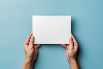 Man holding blank white paper against blue background, minimalistic close up of hands holding an empty white flyer sheet