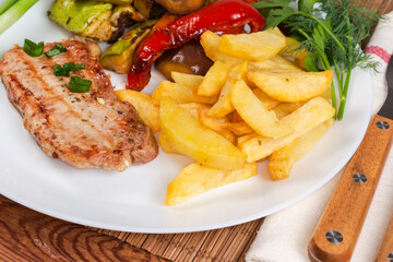 Grilled boneless pork chop with baked vegetables and french fries