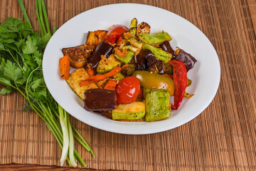 Different baked vegetables on dish and fresh greens on table