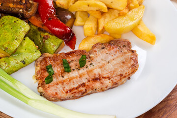 Grilled boneless pork chop against baked vegetables and french fries