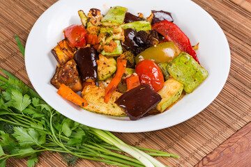 Different baked vegetables on dish and fresh greens on table