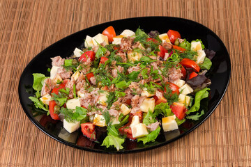 Salad of canned tuna, cheese, fresh vegetables on black dish
