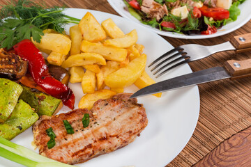Grilled boneless pork chop against baked vegetables and tuna salad