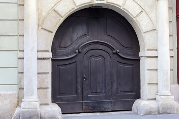 Old wooden gate painted black with wicket in arched passage