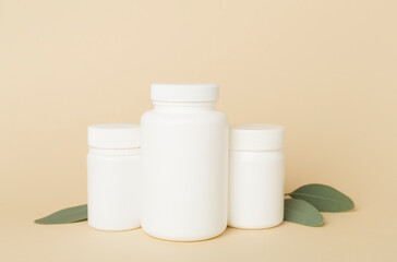 Bottles with pills and green leaves on color background