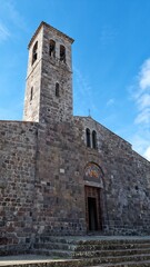 Fototapeta premium Historic stone church with a tall bell tower under a bright blue sky, featuring Romanesque architectural style