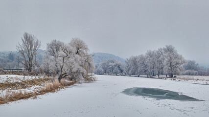 A frozen river on a cold, winter morning. Frost is white on the branches of old willows and dry grass. Low clouds herald snowfall