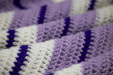 close-up of grandma's retro zigzag striped blanket, in white, lilac or lavender and royal purple, crocheted or knitted, grandma's house, cozy and warm, rippling