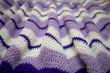close-up of grandma's retro zigzag striped blanket, in white, lilac or lavender and royal purple, crocheted or knitted, grandma's house, cozy and warm, rippling