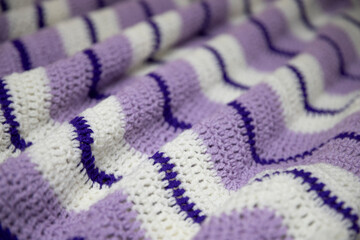 close-up of grandma's retro zigzag striped blanket, in white, lilac or lavender and royal purple, crocheted or knitted, grandma's house, cozy and warm, rippling
