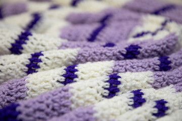 close-up of grandma's retro zigzag striped blanket, in white, lilac or lavender and royal purple, crocheted or knitted, grandma's house, cozy and warm, rippling