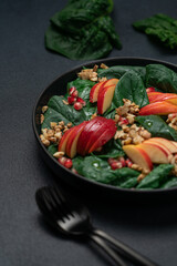 Seasonal salad with pomegranate seeds, walnuts, apples and spinach in a black plate on a dark background, side view