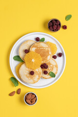Pancakes with orange and raspberries in plate top view on yellow background with copy space. Morning traditional breakfast