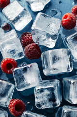 Close-up shot of scattered ice cubes and raspberries. Fresh ice cold juice concept.
