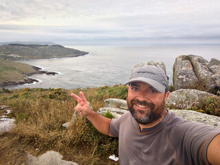 A man in cap taking a selfie on a hill with the sea in the background