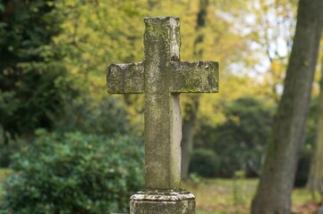 Old stone cross standing in cemetery during autumn