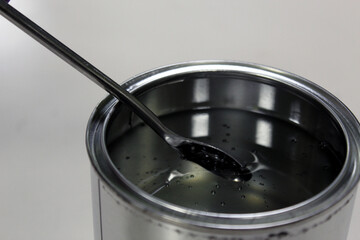 Technician weighing transparent epoxy resin for a paint in a can on a balance by spatula on white background
