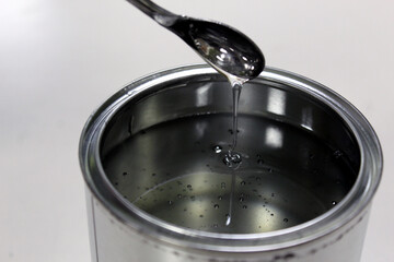Technician weighing transparent epoxy resin for a paint in a can on a balance by spatula on white background