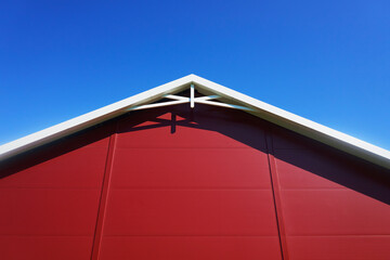 A minimalistic architectural shot capturing the red facade and white beams of a classic building, set against a clear blue sky. This image highlights the elegance of timeless design