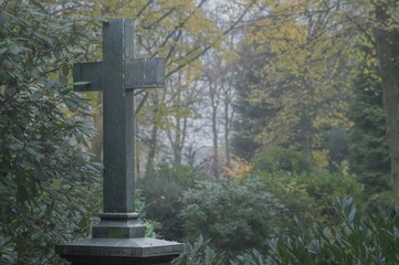 Stone cross standing in a misty cemetery in autumn