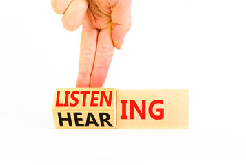 Listening or hearing symbol. Businessman turns wooden cubes and changes a concept word Listening to Hearing. Beautiful white background. Copy space. Business educational listening or hearing concept.