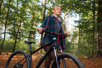 Naklejka premium Young woman with a bicycle in the forest looking away