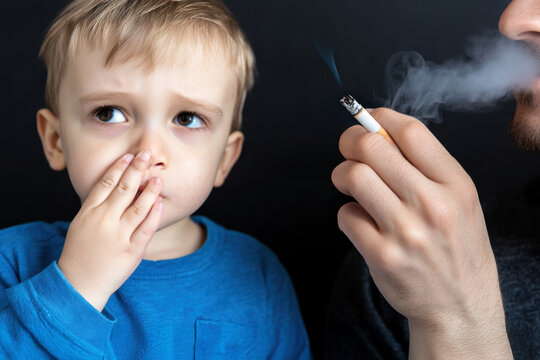 Father smoking near his kid. Unhappy child covers his nose from bad smell of smoke. Bad habits, smoking ban near children, harm of passive smoking. World No Tobacco Day, No Smoking Day background