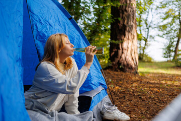 Girl drinks beer while sitting in a tent in the forest © Andrii 