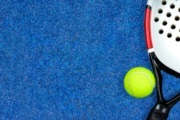 Close-up of a padel ball and racket isolated on the blue court background. Top view and copy space.