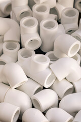 White plastic plumbing pipe fittings in various shapes stacked together. Top view.