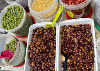 Pickled olives with spices in different colors in containers and buckets at market in Europe, Italy. Organic local food and health. Seasonal vegetables.