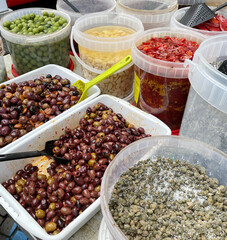 Pickled olives with spices in different colors in containers and buckets at market in Europe, Italy. Organic local food and health. Seasonal vegetables.