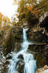 Serene waterfall cascades down moss-covered rocks, surrounded by the vibrant colors of autumn foliage.