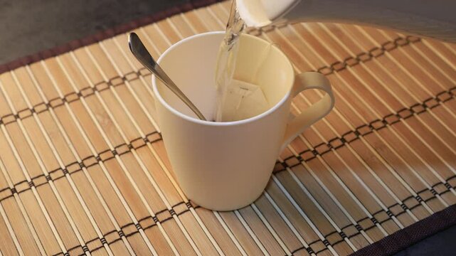 Pouring hot water into a white cup of tea. Close-up. Brewing tea from a tea bag.