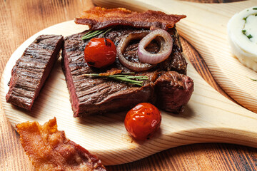 Grilled meat of medium doneness cut with vegetables and cheese on a wooden board and background